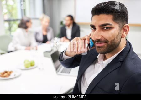 Selbstbewusster Geschäftsmann, der im Konferenzraum über Mobiltelefon oder Smartphone spricht Stockfoto