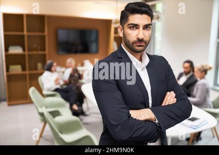 Junger Geschäftsmann mit gekreuzten Armen als selbstbewusste Führungskraft vor dem Team im Büro Stockfoto
