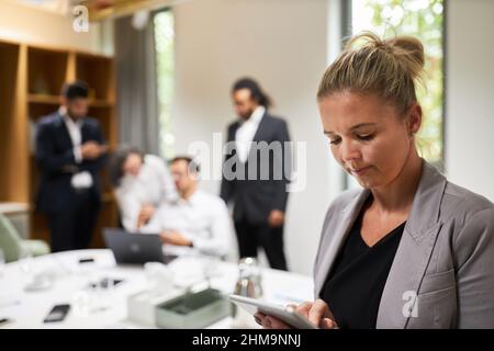 Junge Geschäftsfrau liest oder schreibt Nachricht auf einem Tablet-Computer mit Team auf Hintergrund Stockfoto