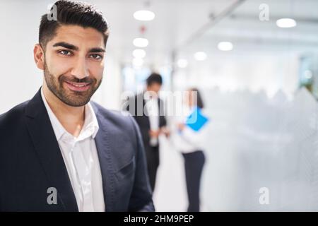 Lächelnder junger Geschäftsmann als Auszubildender oder erfolgreicher Manager auf dem Flur vom Büro aus Stockfoto