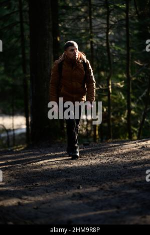 Ein Mann geht im Nebel entlang der Waldwege, die Sonnenstrahlen brechen durch die Bäume und den Nebel, Rucksack auf dem Rücken eines Mannes. Stockfoto