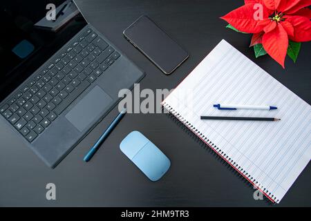 Ein Bild eines Laptop-Tablets, Notizblock mit Mobiltelefon auf einem schwarzen Tisch neben einer roten Blume, bereit zum Lernen oder Arbeiten von zu Hause aus Stockfoto