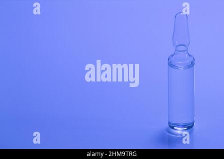 Medizinische Ampulle auf blauem Hintergrund. Glasampulle zur Injektion mit Arzneimittel auf dem Tisch. Konzeptmedikamente und Krankheitsbehandlung. Pharmakologie, Stockfoto