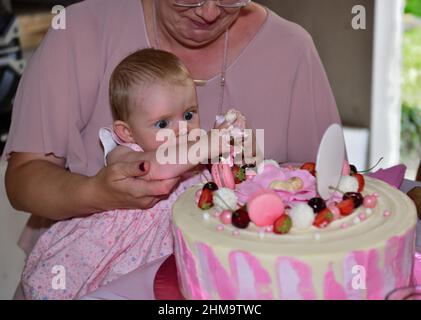 Mädchen neugeborenen 1-jährigen mit Händen berühren Kuchen während der Geburtstagsparty Stockfoto