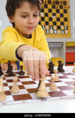 Kaukasischer Junge spielt Schach. Glückliches konzentriertes Kind hinter Schach in der Klasse oder Schulstunde. Aufgeregt clever Grundschule Kind mit Brettspiel Stockfoto