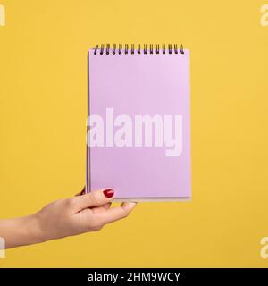 Seitenansicht Nahaufnahme einer Frau, die einen violetten Notizblock in der Hand hält und leeres Papier zeigt. Innenaufnahme des Studios isoliert auf gelbem Hintergrund. Stockfoto
