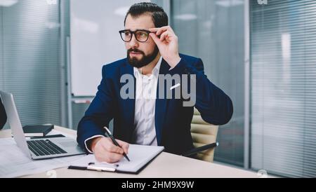 Nachdenklicher Geschäftsmann, der in einem modernen Arbeitsbereich arbeitet Stockfoto