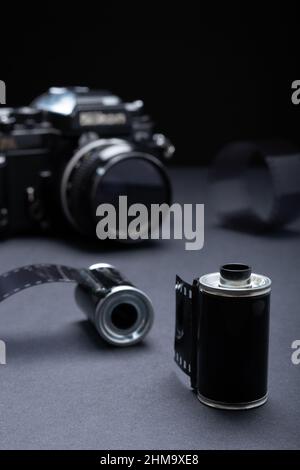 Filmfotografie - eine Vintage-Metallic-Filmkassette und 35mm SLR-Kamera vor dunklem Hintergrund. Stockfoto