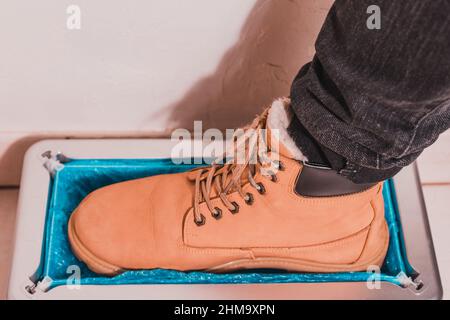 Gerät für die automatische Verkleidung von Stiefelabdeckungen, ein Mann in braunen Schuhen legt Stiefelabdeckungen, mechanische clintoper an. Stockfoto