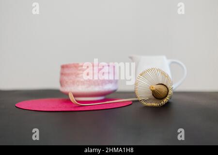 Keramikschale und hölzerne Chasen und Chaschaku auf rosa runden Stand auf schwarzem Tisch bei Sonnenlicht Stockfoto