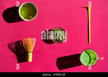 Draufsicht auf hellen Hintergrund von Glas grünem Tee und getrockneten Matcha mit Bambus Chasen und Chaschaku auf rosa Oberfläche Stockfoto