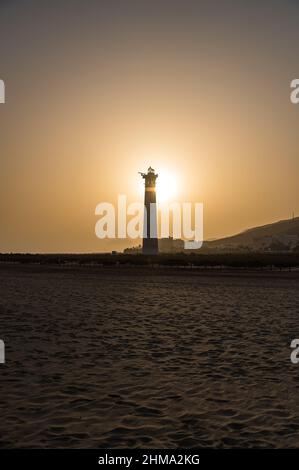 Friedliche Landschaft mit der Silhouette eines Leuchtturms an der hügeligen Küste gegen den Sonnenuntergang am Sommerabend Stockfoto