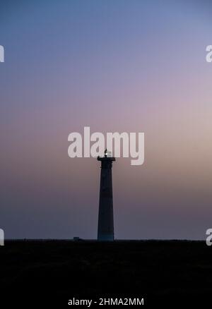 Szenischer Blick auf den Turm des Leuchtfeuers, der vor dem Hintergrund des Sonnenuntergangs am Meer leuchtet Stockfoto