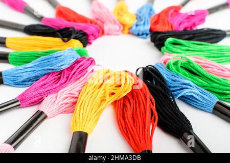 Viele gemischte bunte Nähfäden zum Sticken in einem Kreis isoliert auf einem weißen Tisch, Seitenansicht von rot, rosa, gelb, blau, schwarz und dargestellt Stockfoto