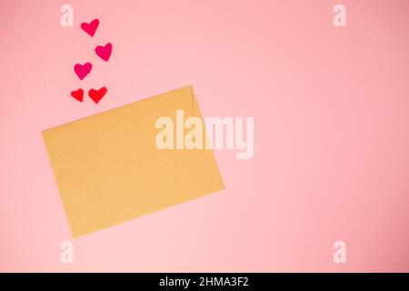 Ein Umschlag aus Kraftpapier mit aus Filz geschnittenen Herzen. Rosa Hintergrund. Speicherplatz kopieren. Modell. Valentinstag-Konzept. Stockfoto