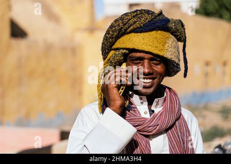 Entzückte ägyptischen Mann in Turban in der Straße an sonnigen Tag stehen und mit einem Anruf, während Blick auf die Kamera Stockfoto