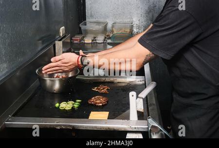 Seitenansicht des anonymen Gemüts, der in der Restaurantküche steht und Zutaten für den Burger zubereitet Stockfoto