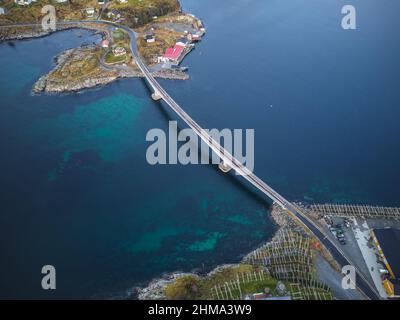 Drohnenansicht einer langen schmalen Brücke über das ruhige klare Meer auf grasbewachsenen Lofoten-Inseln mit Gebäuden in der Natur Norwegens Stockfoto