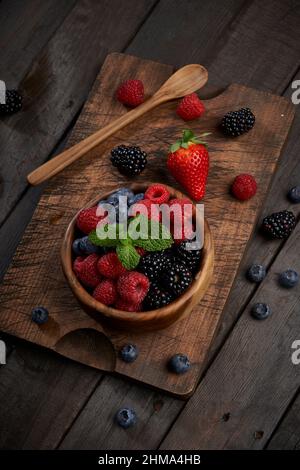 Von oben Schale mit verschiedenen reifen Beeren und Minzblättern auf Holzschneidebrett in heller Küche Stockfoto
