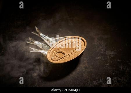 Von oben von Fischkonserven in Zinndose mit geöffneter auf schwarzem Hintergrund mit Rauch im Raum mit gedämpftem Licht platziert Stockfoto
