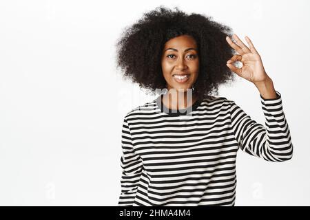 Okay, Sehr gut. Lächelndes afroamerikanisches Frauenmodell, zeigt ok, Null-Geste, Lob smth, Kompliment, Empfehlen brad oder Geschäft, weiß Stockfoto