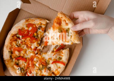 Weibliche Hand nehmen Stück mexikanische Pizza in Karton für die Lieferung auf weißem festem Hintergrund. Draufsicht Stockfoto