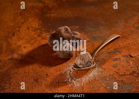 Von oben Zusammensetzung auf kleinen Metalllöffel mit köstlichen köstlichen Schokoladentrüffel und Kakaopulver auf rostige Oberfläche gelegt Stockfoto