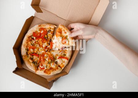 Weibliche Hand nehmen Stück mexikanische Pizza in Karton für die Lieferung auf weißem festem Hintergrund. Draufsicht Stockfoto