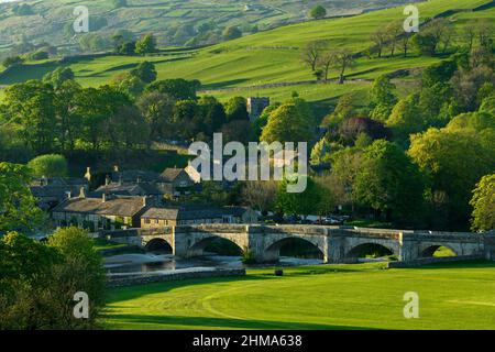 Landschaftlich schöner, sonniger Burnsall, eingebettet in das Tal (5-gewölbte Brücke, attraktive Hütten, Kirchturm, grüne Hangfelder) - Yorkshire Dales, England, Großbritannien. Stockfoto