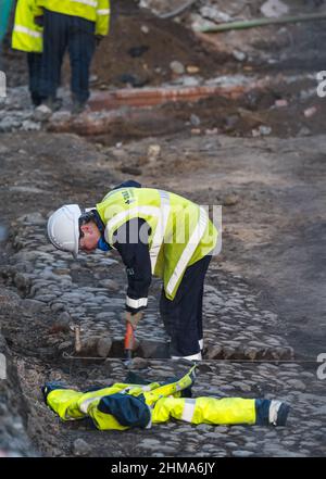 Leith, Edinburgh, Schottland, Großbritannien, 8th. Februar 2022. Straßenbahnen nach Newhaven Bau: Da sich das Großprojekt dem letzten Jahr nähert, die Arbeiten termingerecht und im Frühjahr 2023 im Rahmen des Budgets von £207,3m fertiggestellt werden, sind in Leith zahlreiche Straßen für den Verkehr gesperrt. Mehr als 60 % der Gleise wurden nun verlegt (2,8km) und 85 % der Umleitungen der Versorgungsunternehmen wurden durchgeführt. Im Bild: Eine Frau gräbt zwischen alten Kopfsteinpflaster in der Constitution Street Stockfoto