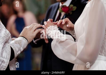 Hände von Braut und Bräutigam in feierlichem Prozess des Austausches von Ringen, symbolisiert die Schaffung einer neuen glücklichen Familie. Bräutigam legt einen Ring auf den Finger der Braut d Stockfoto