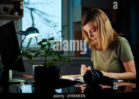 Frau, die im Home Office am Tisch sitzt und mit dem Computer arbeitet. Freiberuflicher Mitarbeiter, der verspätet arbeitet. Emotionaler Stress und Burnout Stockfoto