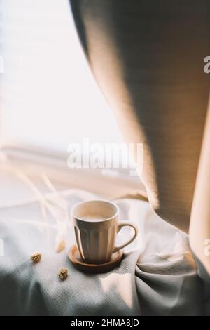 Tasse Kaffee mit Milch auf beigefarbenem Textil. „Still Life“-Frühstückskonzept. Warme und komfortable Atmosphäre Foto in hellen Pastellfarben. Stockfoto