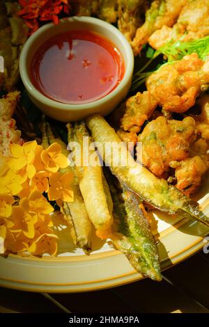 Frittierte tropische Blumen, Blätter und Gemüse auf einem weißen Teller serviert, flach auf dem Bambustisch. Gesunde Ernährung. Draufsicht. Nahaufnahme. Stockfoto