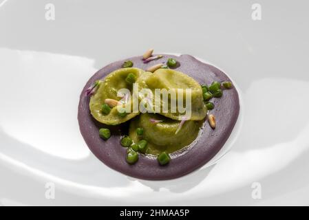 Grüner Spinat Tortelloni gefüllt mit Käse und Gemüse, auf Rote Bete Püree mit Erbsen und Pinienkernen, Nahaufnahme Stockfoto