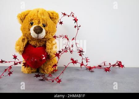Eine Teddybärpuppe, die ein herzförmiges Kissen mit Liebe hält Stockfoto