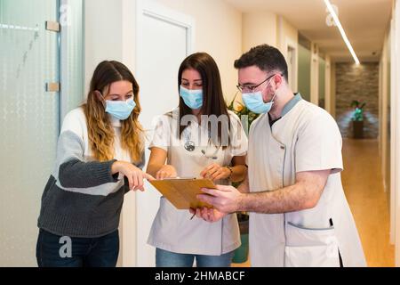 Die Ärztin und ihre medizinische Assistentin helfen einem Patienten, ein Formular in einem Gesundheitszentrum auszufüllen. Stockfoto