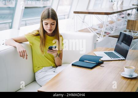Student stöbert im Café auf sein Mobiltelefon Stockfoto