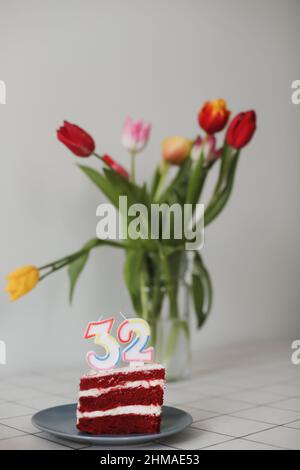 Geburtstagskuchen mit 32-Nummern-Kerze mit einem Blumenstrauß in einer Vase auf dem Hintergrund Stockfoto