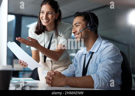 Zufriedene Kunden sind das Herz eines erfolgreichen Unternehmens. Aufnahme eines jungen Mannes und einer jungen Frau, die während der Arbeit in einem Callcenter ein Dokument lesen. Stockfoto