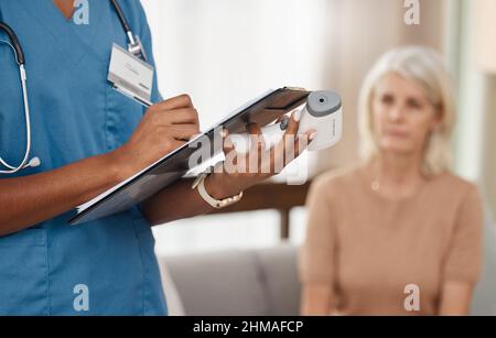 Aus dem Haus eine Gesundheitseinrichtung. Aufnahme eines Arztes, der während einer Konsultation mit einer älteren Frau zu Hause einen Fragebogen ausfüllt. Stockfoto