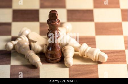 Gefallene Schachfiguren, die um einen König auf einem Schachbrett liegen. Licht scheint von der rechten Seite Stockfoto