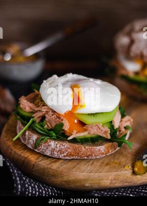 Pochiertes Ei auf einem Vollkornbrötchen mit Avocado, Gurke, Kiwi und Rucola auf einem grauen Teller. Gesundes Frühstück. Brunch-Idee. Sauberes Essen. Vegetarisch. pr Stockfoto