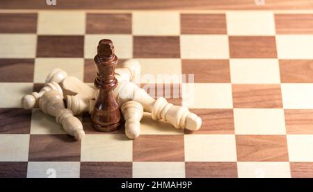 Gefallene Schachfiguren, die um einen König auf einem Schachbrett liegen. Licht scheint von der rechten Seite Stockfoto