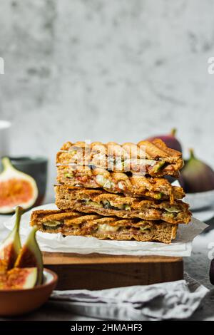 Gesundes, natürliches Sommerfutter. Sandwiches mit Vollkornbrot, Prosciutto, Feigen und Brie-Käse auf Holzbrettservietten auf grauem Grund. Gesund Stockfoto