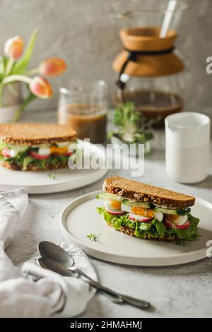 Gesundes, natürliches Frühlingsfrühstück oder Brunch. Servieren von Sandwiches mit Vollkornbrot, Avocado, Eiern, Rettich, Gurken-Ion-Weißteller mit Kaffee Stockfoto