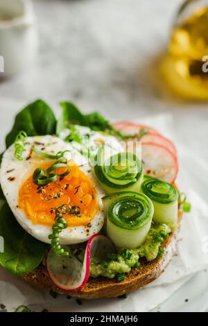 Gesundes, natürliches Sommerfutter. Serviert Sandwiches mit Vollkornbrot, Avocado, Eiern, Rettich, Gurke auf weißem Brett und weißem Hintergrund. Mittagessen Stockfoto