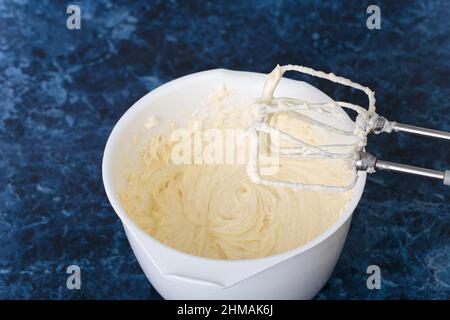 Die Zutaten für den Käsekuchen werden gemischt. Käsekuchen machen Prozess. Blauer Marmorhintergrund. Nahaufnahme. Stockfoto