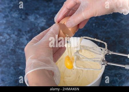 Das Ei wird dem Käsekuchen-Teig hinzugefügt. Käsekuchen machen Prozess. Blauer Marmorhintergrund. Nahaufnahme. Stockfoto