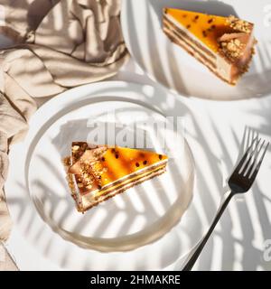 Mehrschichtiger Kakao-Biskuitkuchen, Mango-Fruchtfüllung und cremige Quark-Creme auf einem hellen Hintergrund mit Schatten. Stockfoto